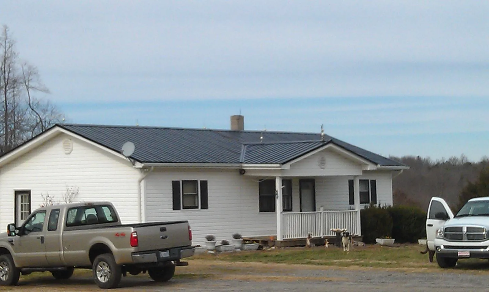 Finished dark metal roof on a white ranch home with work trucks parked in Troy